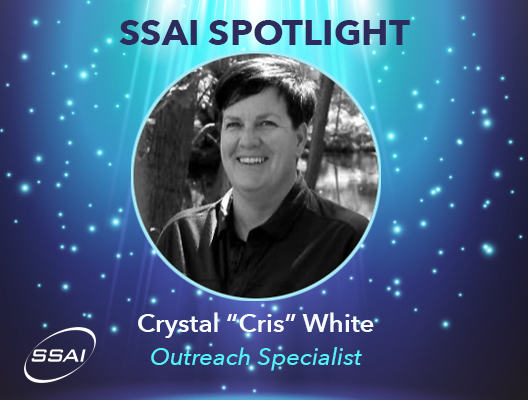 Black and white portrait photo of Crystal White. Her picture is in a frame with stars around it and spotlights from the top. Her name and title, Outreach Specialist, appear under her name and the words SSAI Spotlight are at the top of the frame. There is an SSAI logo in the bottom left corner.